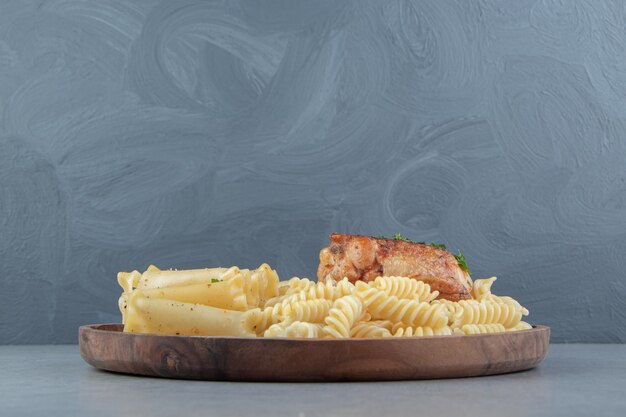 Variety of pasta with grilled chicken on wooden plate.