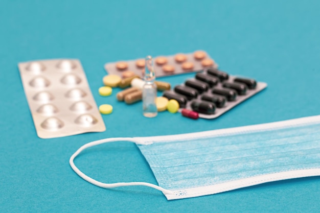 Free photo a variety of pills and a protective face mask on a blue background