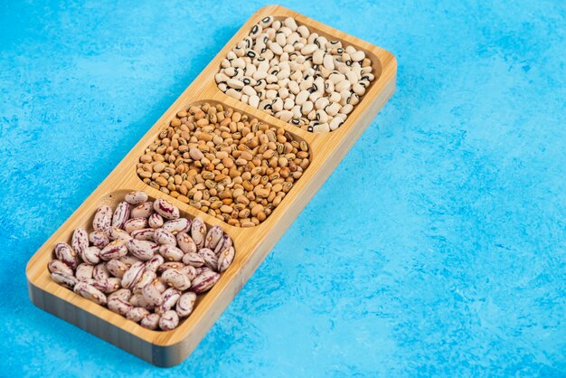 Variety of raw beans on wooden plate.