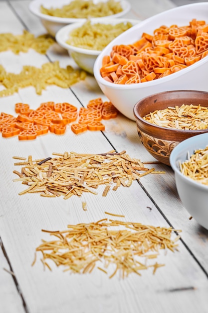 Free photo variety of uncooked pasta bowls on wooden table.