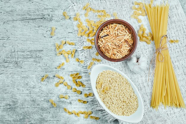 Variety of uncooked pasta with garlic and white tablecloth.