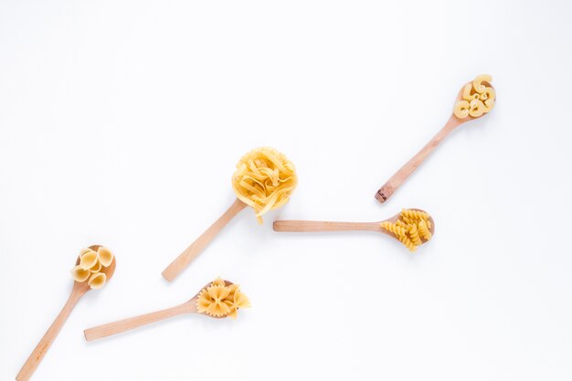 Variety of uncooked whole wheat italian pasta on wooden spoon isolated over white backdrop