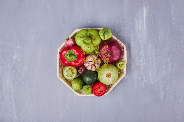 Variety of vegetables in a bamboo basket in the middle on blue table.