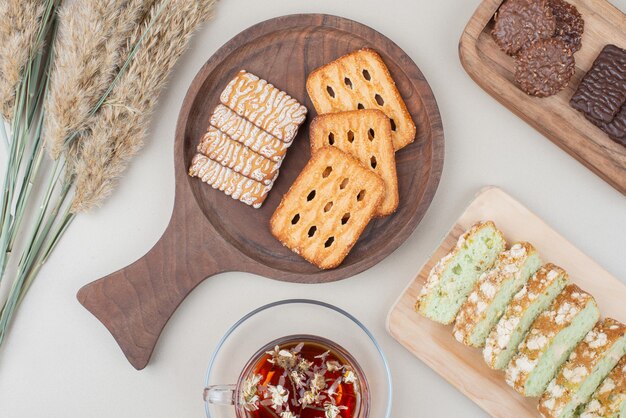 Various biscuits, cake slices and cup of tea on white surface