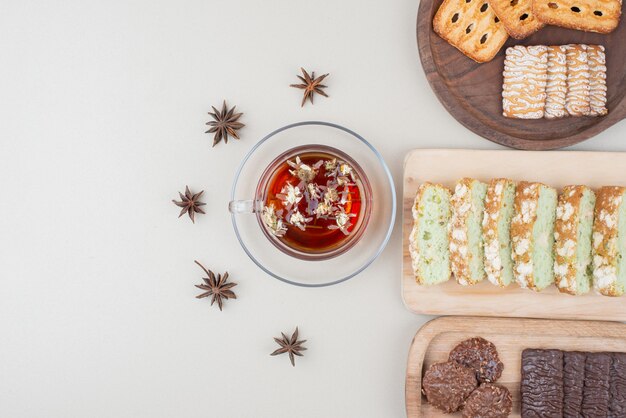 Various biscuits, cake slices and cup of tea on white surface