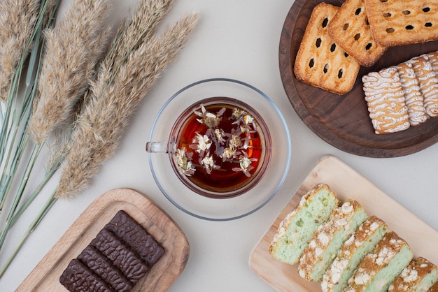 Various biscuits, cake slices and cup of tea on white.