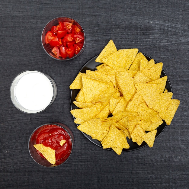 Various bowls with nachos tomatoes red and white sauces 