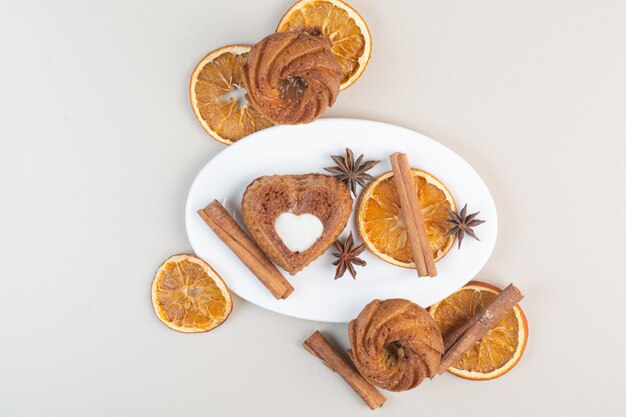 Various cakes with orange slices, cloves and cinnamon on white plate