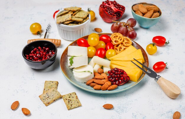 Различный сыр и сырная тарелка на светлом столе с разными орехами и фруктами