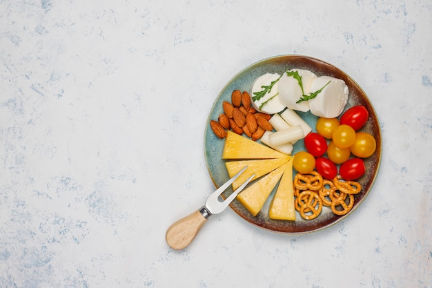 Различный сыр и сырная тарелка на светлом столе с разными орехами и фруктами