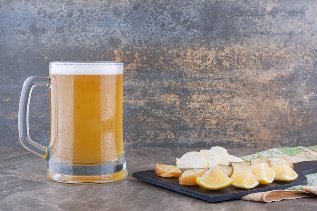 Various cheese and lemon slices on dark board with beer