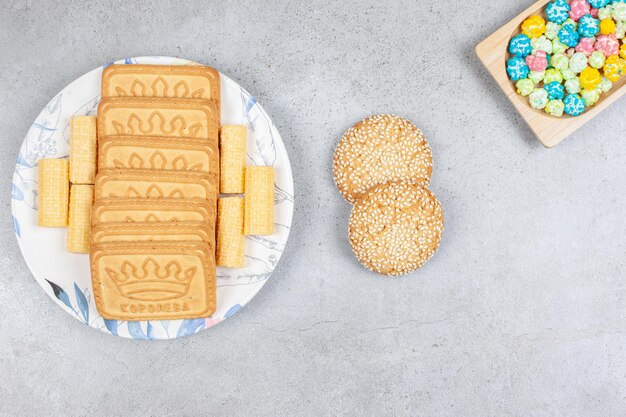 Различное печенье на тарелке с двумя печеньями рядом с конфетами на мраморном фоне. Фото высокого качества