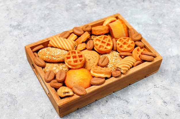 Various cookies in a wooden tray on gray surface