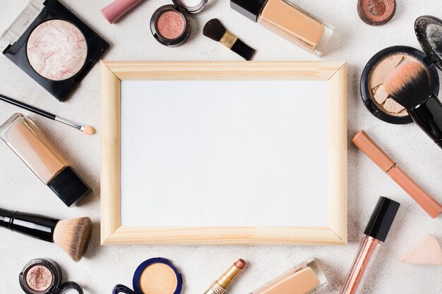 Various cosmetics and blank frame scattered on light background