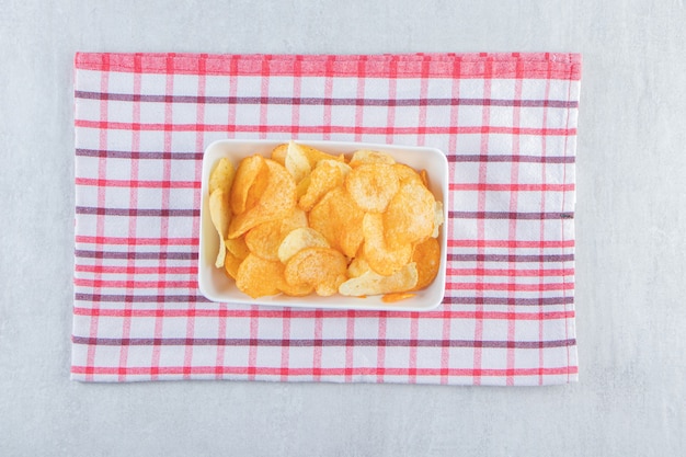 Various crispy chips placed in white bowl with tablecloth.