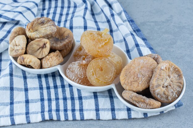 Various dried fruits in the bowl, on the tea towel, on the marble table. 