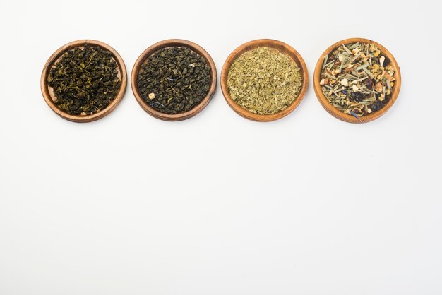 Various dried meadow herbs tea on wooden circular plate against white background