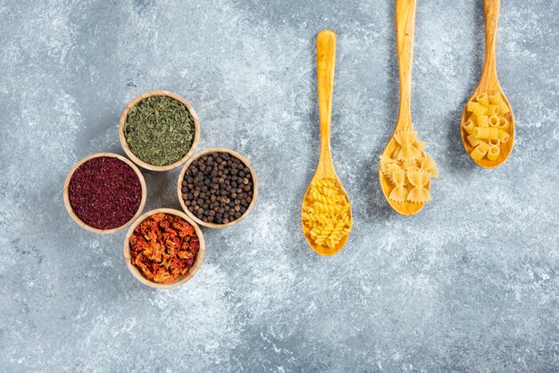 Various dry pasta and spices on marble background.