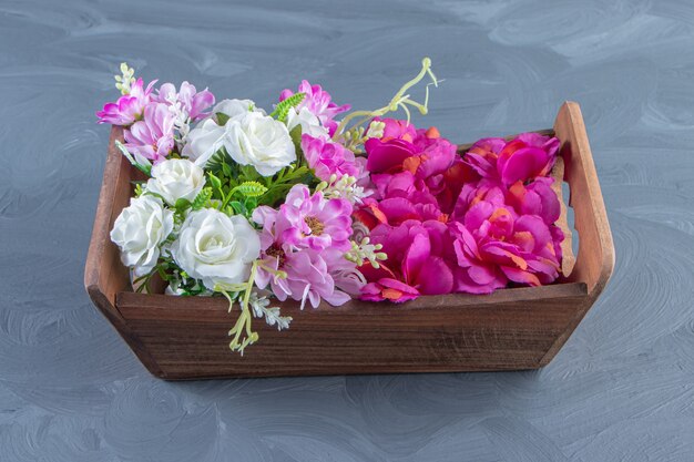 Various flowers in a box, on the white table.