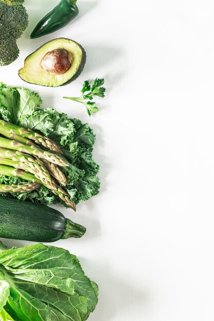 Various fresh green vegetables on a white background broccoli celery avocado zucchini kale parsley hot pepper lettuce leaves Healthy vegetarian food concept background