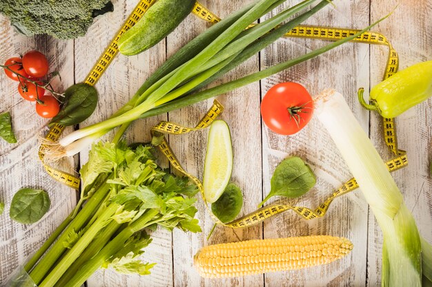 Various fresh green vegetables with measuring tape on wooden surface