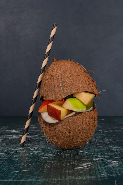 Various fruits in half cut coconut with straw on marble table