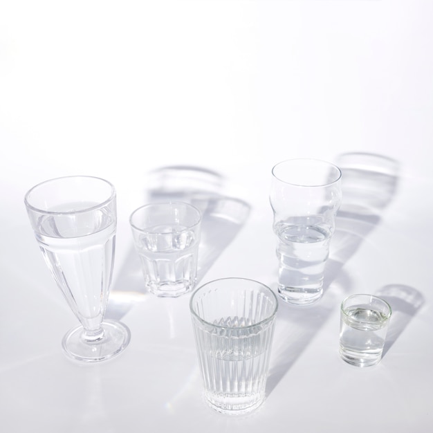 Various glasses of water with shadow on white background