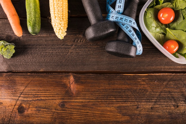 Various healthy food with measuring tape and dumbbell on wooden backdrop
