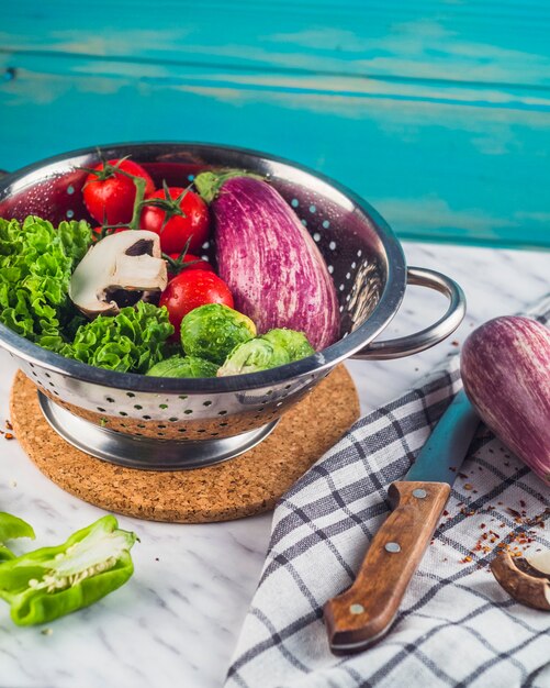 Various healthy vegetables in colander over marble tabletop