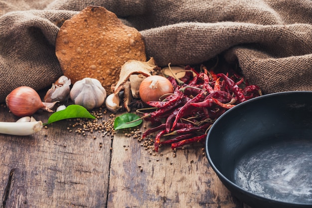 Various ingredients used to make Asian food are placed beside the pan on the wooden table.