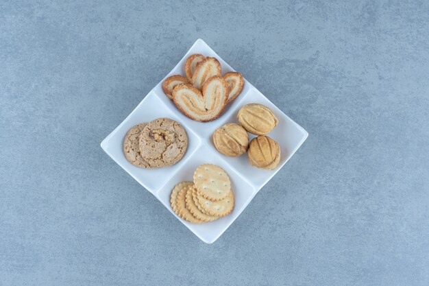 Various kinds of cookies on white plate over grey background.