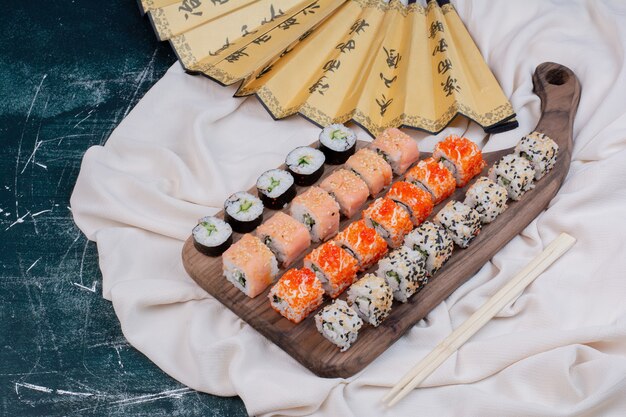 箸と扇子が付いた木製の大皿に、さまざまな種類の巻き寿司が添えられています。