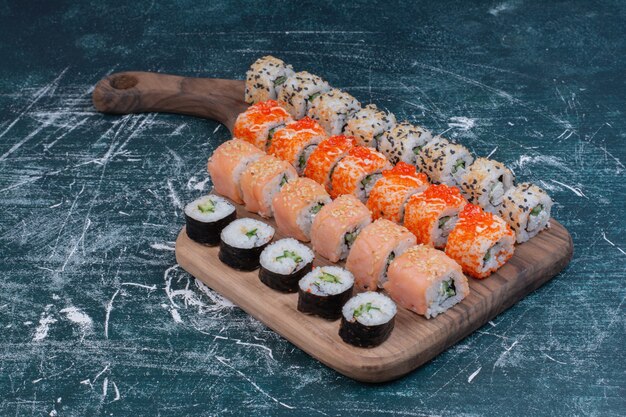 Various kinds of sushi rolls served on wooden platter.