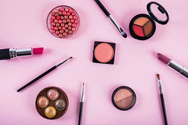 Various makeup and cosmetic products on pink backdrop