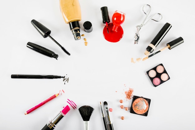 Various makeup products forming circular frame on white background