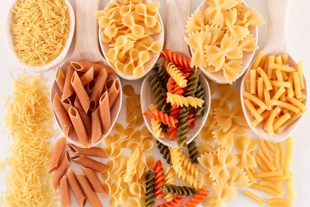 various mix of pasta on wooden white surface top view