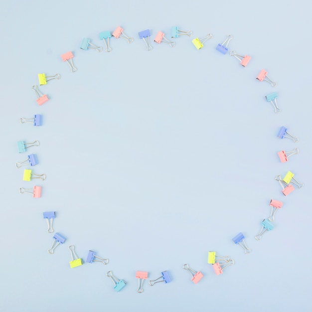 Various multi colored bulldog clips forming circle on blue backdrop