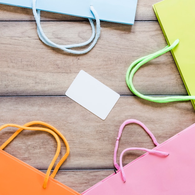 Vari multi colorati sacchetti della spesa con la carta bianca in bianco sullo scrittorio di legno