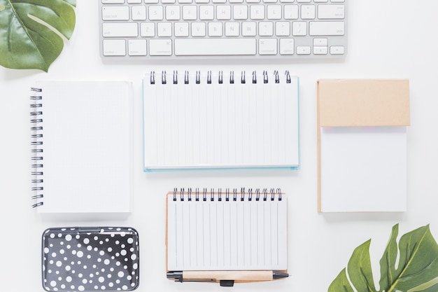 Various notebooks and keyboard on white desk