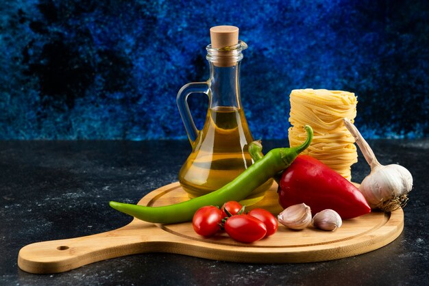 Various pasta, oil and vegetables on wooden board.