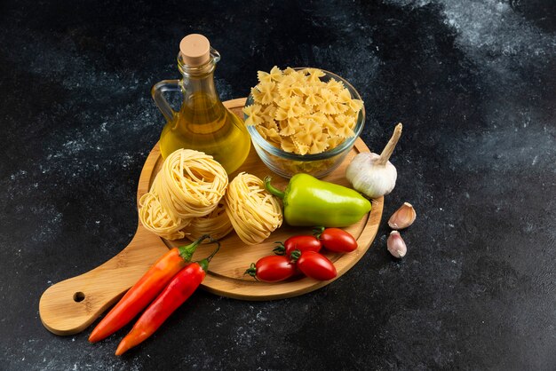 Различные макаронные изделия, масло и овощи на деревянной доске.