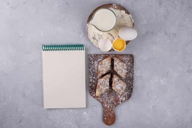 Various pastries and ingredients on the wooden platter with a notebook aside