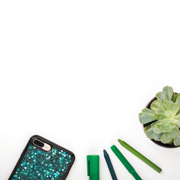Various pens with smartphone and potted plant on white background