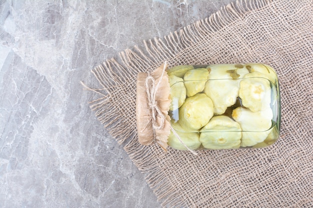 Various pickled vegetables in glass jar on burlap.