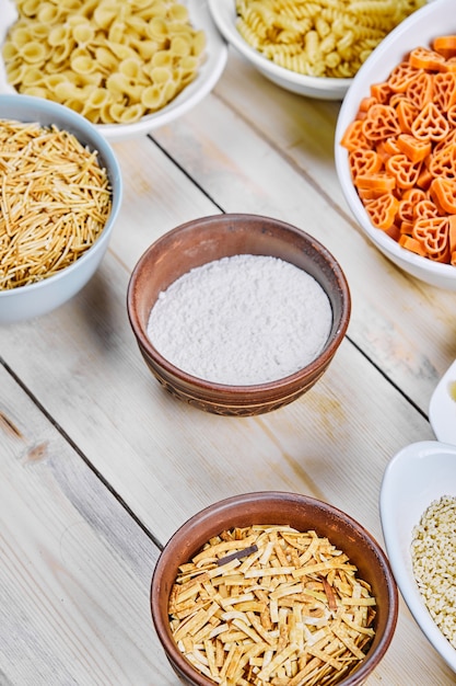 Various raw pasta and flour bowl on wooden table.