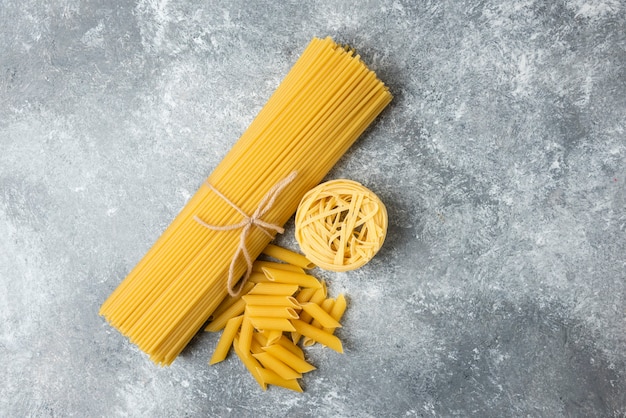 Various raw pasta on marble background. Spaghetti, penne, tagliatelle. 