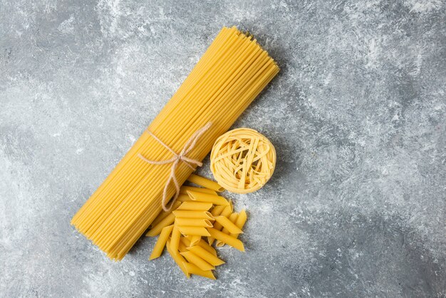 Various raw pasta on marble background. Spaghetti, penne, tagliatelle. 