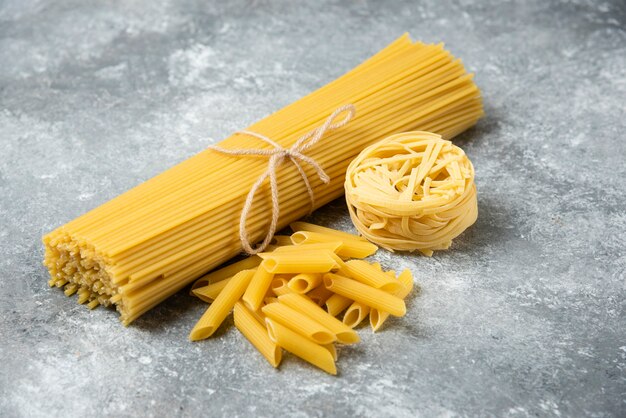 Various raw pasta on marble surface. Spaghetti, penne, tagliatelle. 