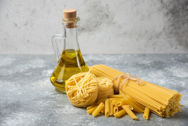 Free photo various raw pasta with bottle of olive oil on marble table.