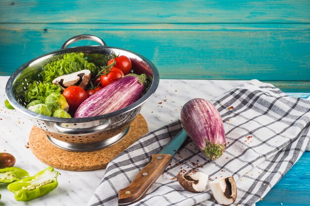 Various raw vegetables in colander over marble desk